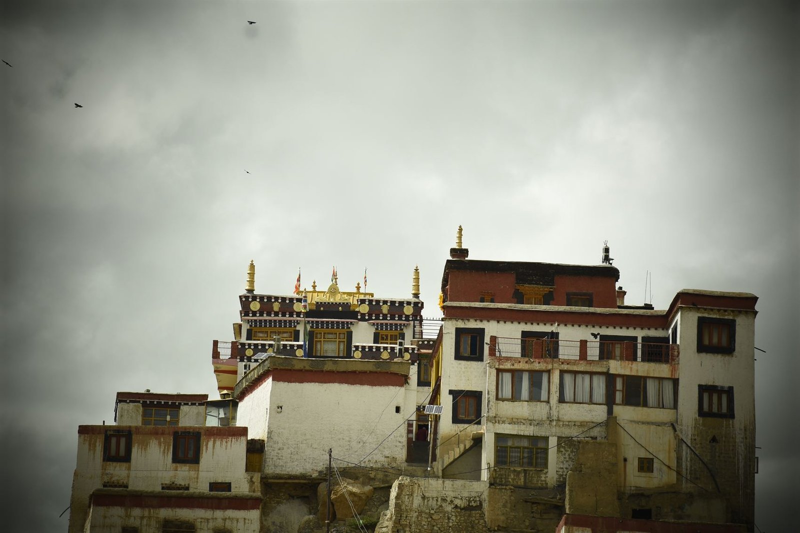 A whitewashed monastery built into a cliffside under a stormy sky